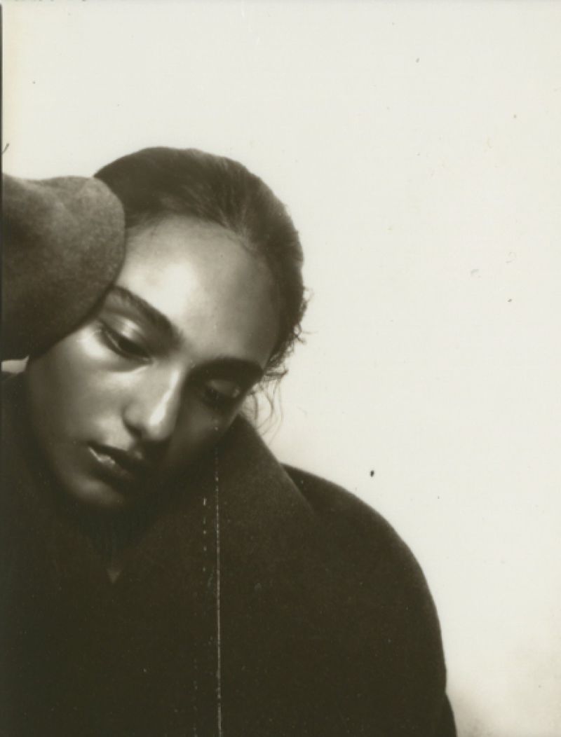 Monochrome portrait of a woman in a dark coat and hat, gazing downward with a serene expression against a plain white background.
