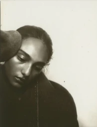 Black and white portrait of model Sofia Subramaniam wearing a dark coat looking downward against a pale studio backdrop.