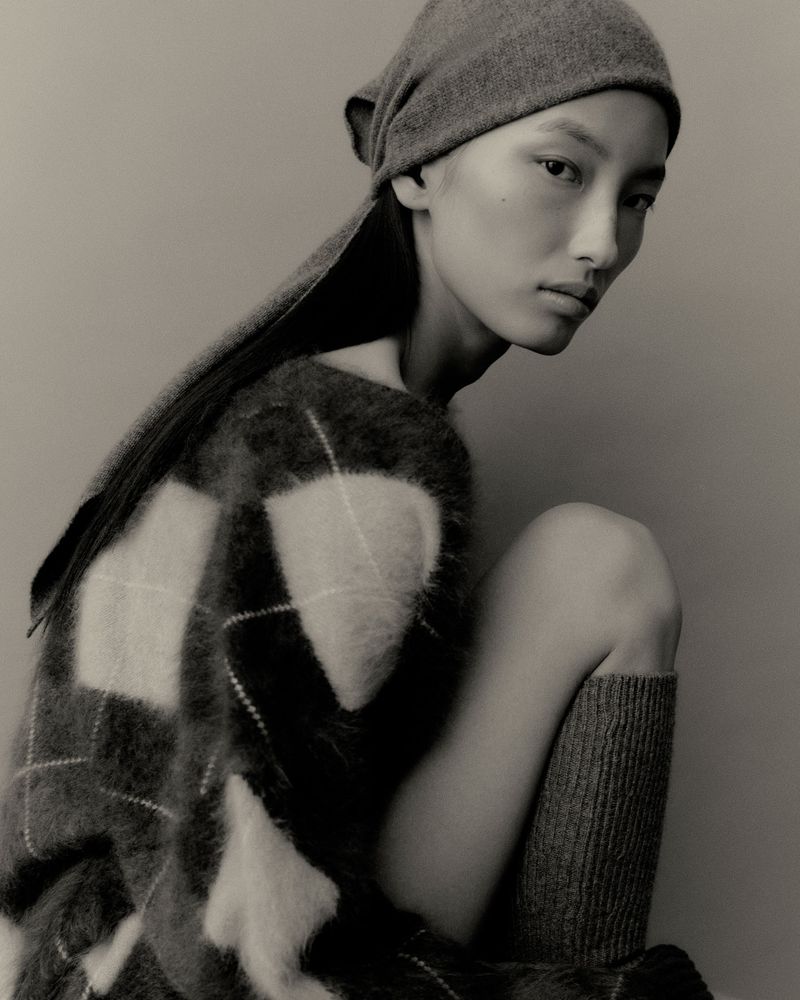 Model wearing a patterned sweater and matching head wrap against a neutral grey studio background for Lisa Yang Fall 2025.