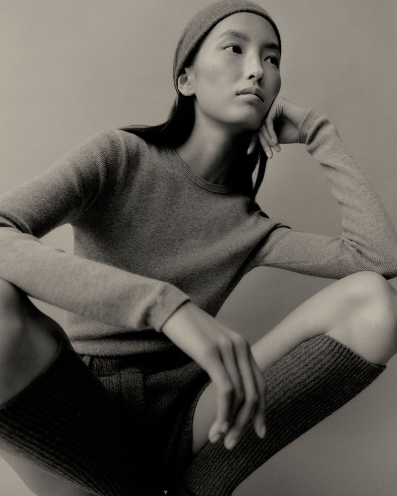 Model wearing a matching knit top and beanie, crouching against a solid grey background for Lisa Yang Fall 2025.