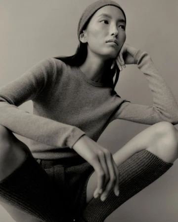 Model wearing a matching knit top and beanie, crouching against a solid grey background for Lisa Yang Fall 2025.