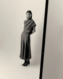 Model wearing a draped knit top and long skirt against a plain studio background