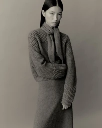 Model wearing a textured knit sweater and matching skirt with a scarf against a neutral studio backdrop
