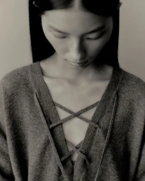 Close-up portrait of a model wearing a grey knit sweater with lace-up neckline details against a neutral background.