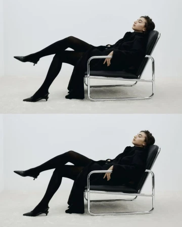 A woman in black attire is elegantly reclined in a chair against a white backdrop, showcasing a blend of fashion and minimalist style.