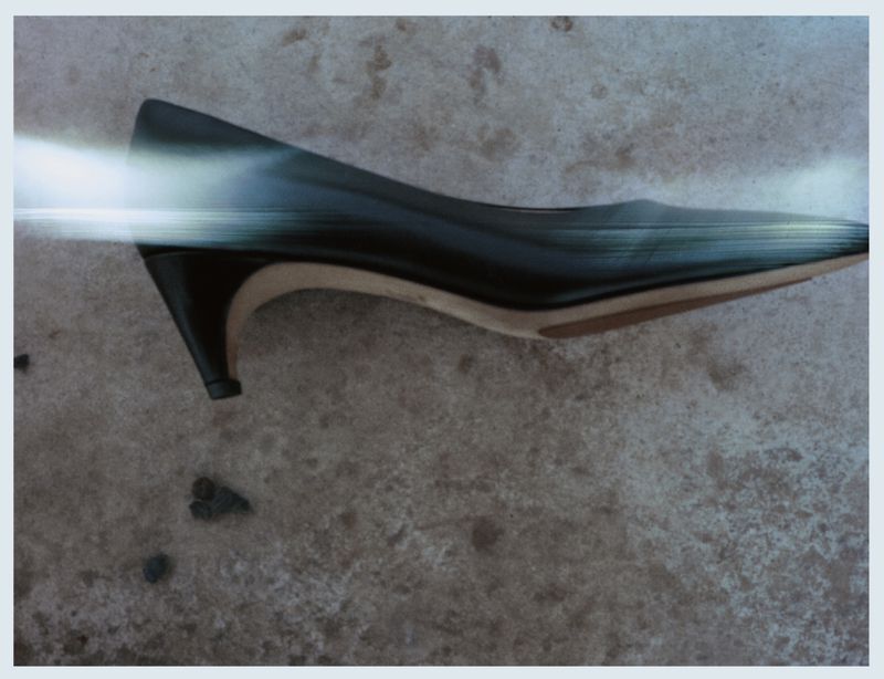 Close-up of a single black, leather heeled dress shoe resting on mottled grey surface with a digitally imposed blurred streak across it.