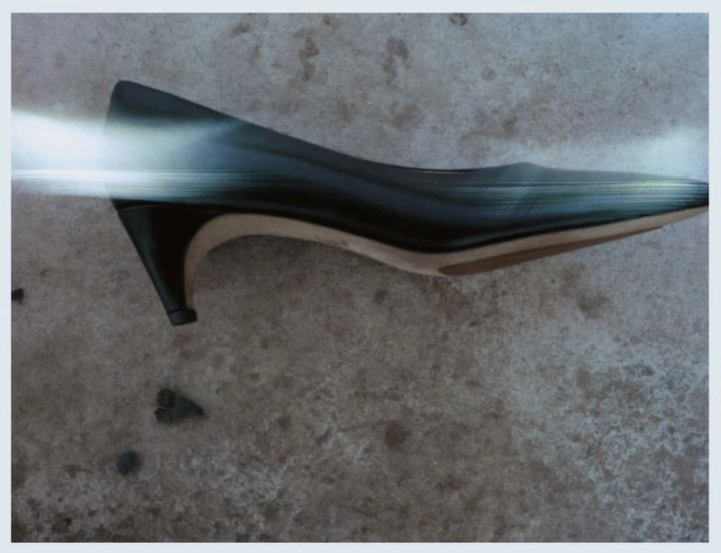Close-up of a single black, leather heeled dress shoe resting on mottled grey surface with a digitally imposed blurred streak across it.