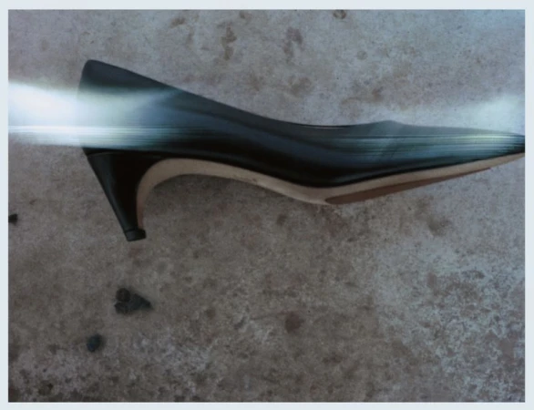Close-up of a single black, leather heeled dress shoe resting on mottled grey surface with a digitally imposed blurred streak across it.