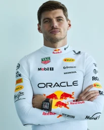 Max Verstappen wearing a white racing suit with sponsor logos and a black wristwatch against a light background