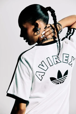 Profile view of a woman with dark hair in a braid wearing an Adidas t-shirt, silver earrings, and rings, with her hand on her neck.