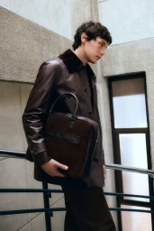 Model wearing a dark brown leather jacket holding a matching leather briefcase on a staircase for Desa