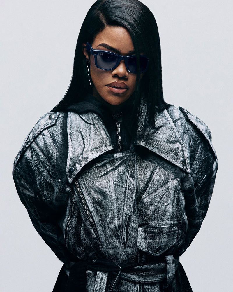 Portrait shot of a stylish adult woman wearing dark sunglasses and a gray jacket in front of a neutral studio backdrop. Fashion.