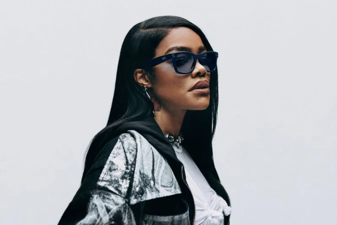 Portrait of Teyana Taylor wearing dark sunglasses and a patterned jacket against a white background