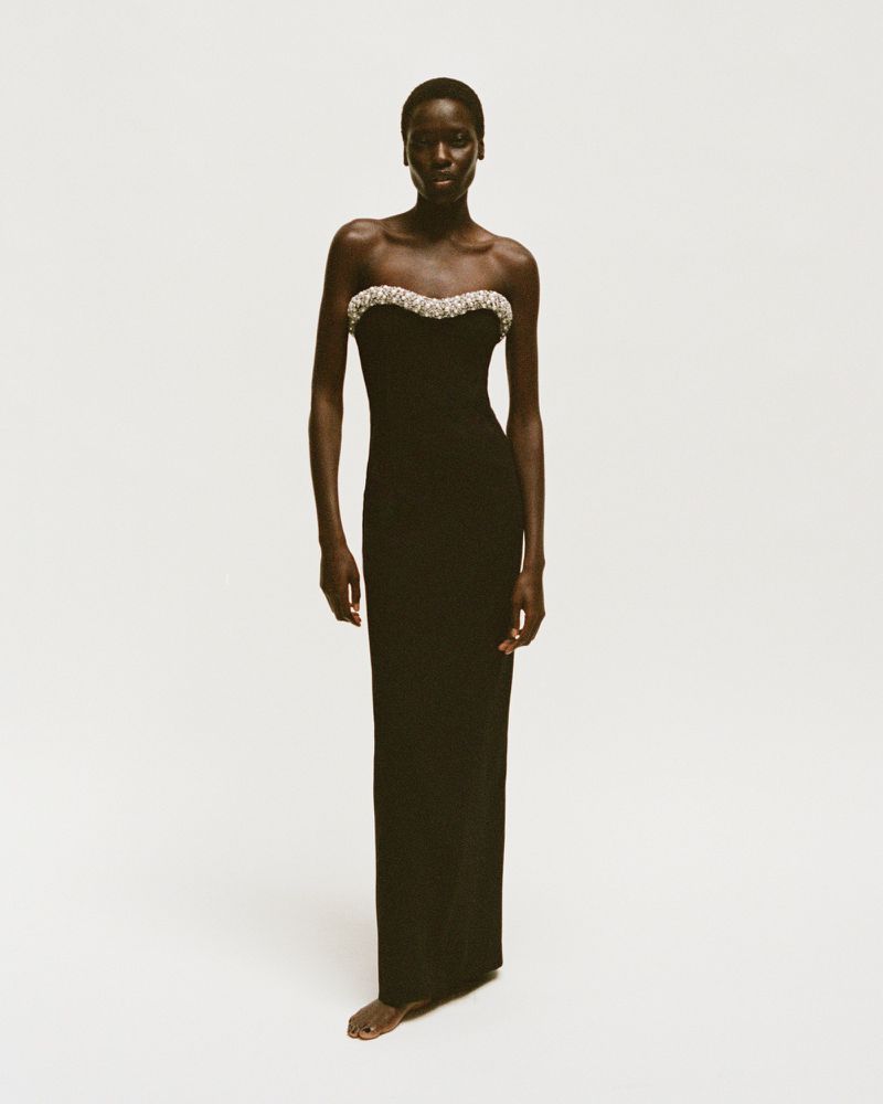 Full-length portrait of a Black female model in a fitted black strapless gown with a beaded sweetheart neckline, set against a white backdrop.