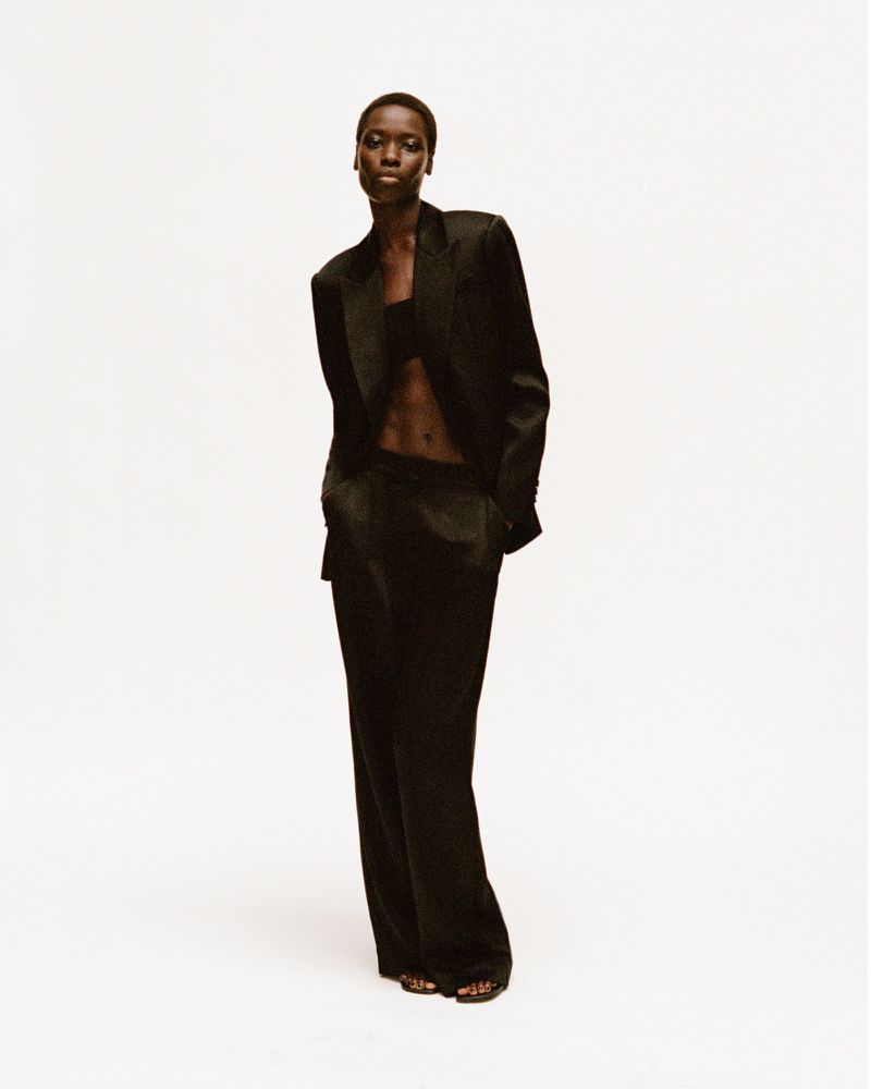 Model Awar Odhiang in a black suit by Simkhai standing against a white seamless backdrop.