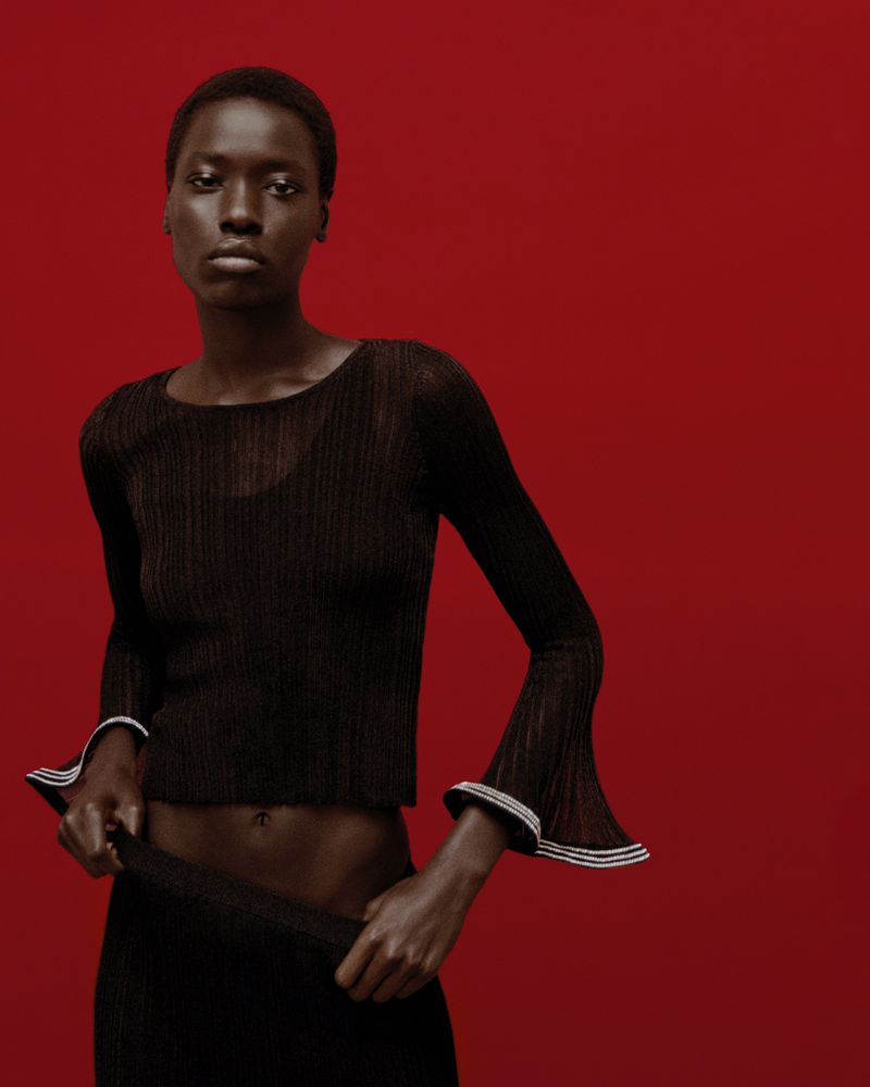 A striking studio shot features a Black female model in a black top and skirt against a vibrant red backdrop, showcasing fashion and beauty.