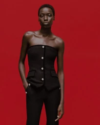 Model Awar Odhiang in a black strapless top against a solid red background for Simkhai Holiday 2025