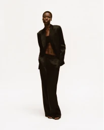 Model Awar Odhiang in a black suit by Simkhai standing against a white seamless backdrop.