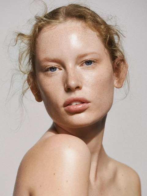 Close-up studio portrait of a young adult woman with freckles and blue eyes looking at the camera with a neutral expression.