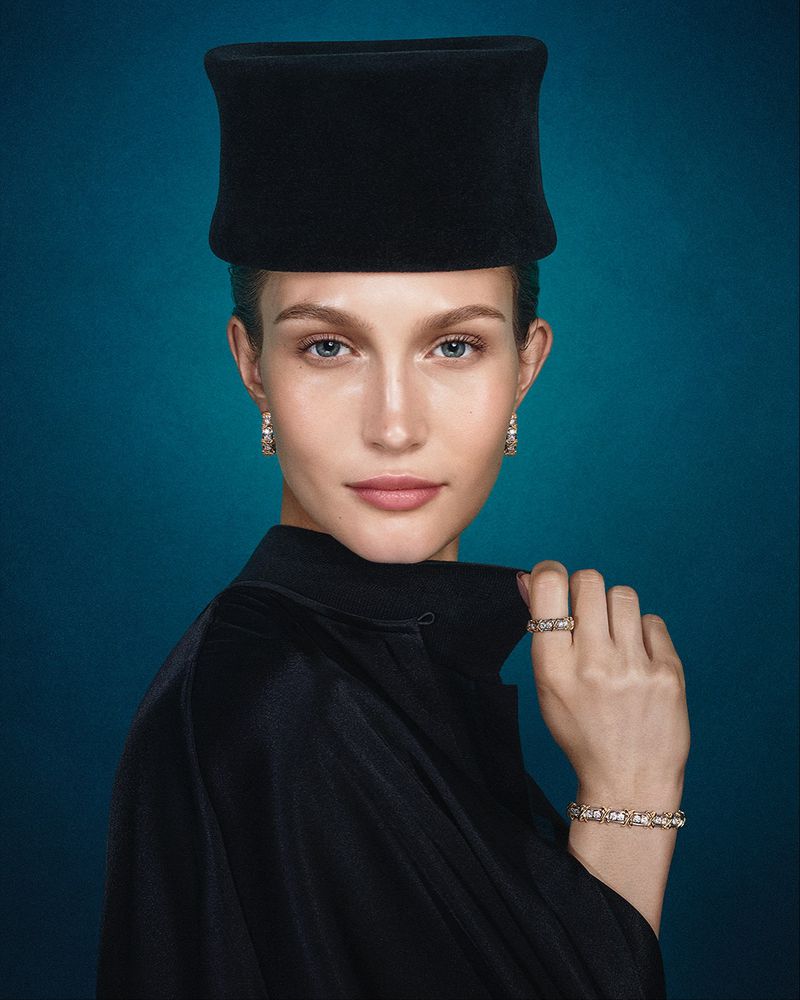 Elegant woman with black hat and jewelry on a blue background, showcasing sophistication and classic style.