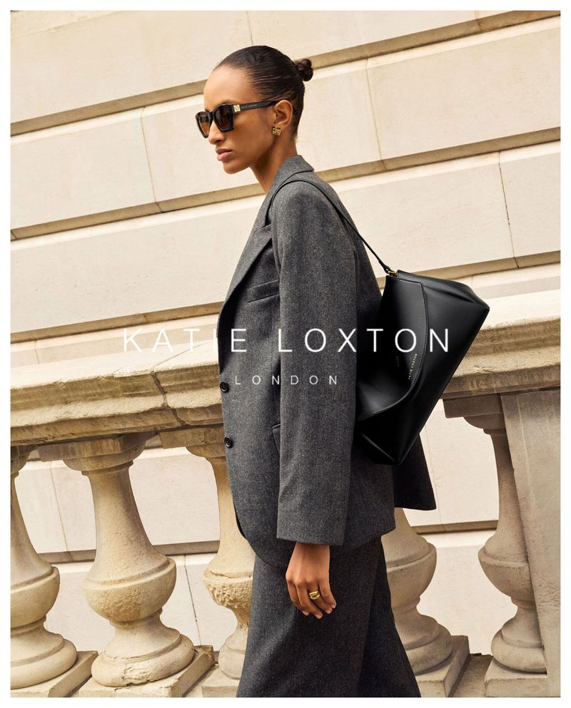 Model in grey wool suit wearing dark sunglasses carrying a black handbag outdoors