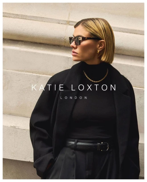 Stylish woman with blonde bob haircut wearing sunglasses, black top and coat posing in front of a stone wall with text overlay.
