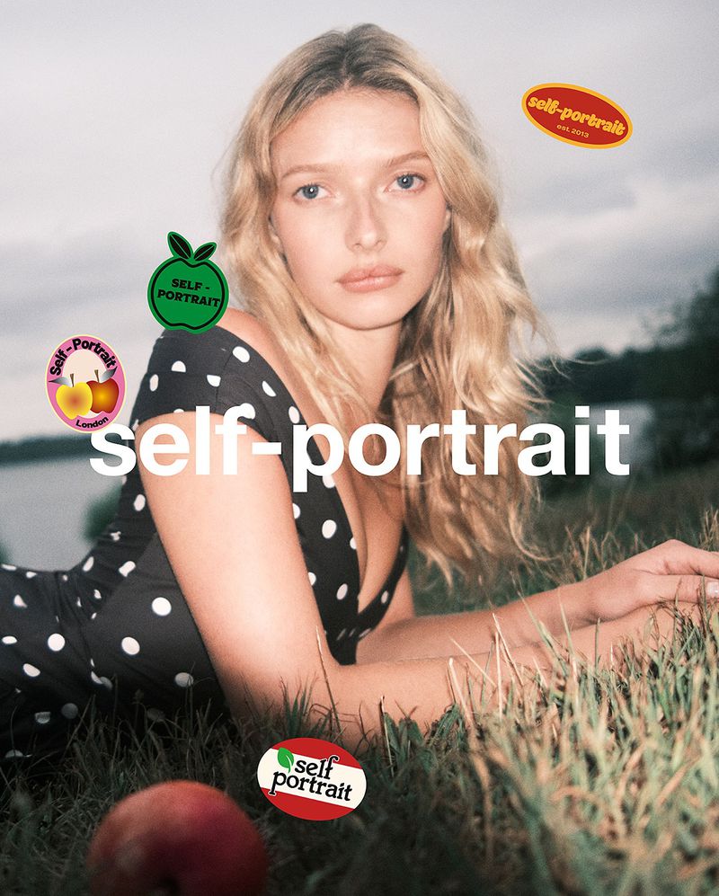 Blonde woman lies in grass wearing polka dot dress in a fashion editorial with vintage sticker graphics and a lake in the background.