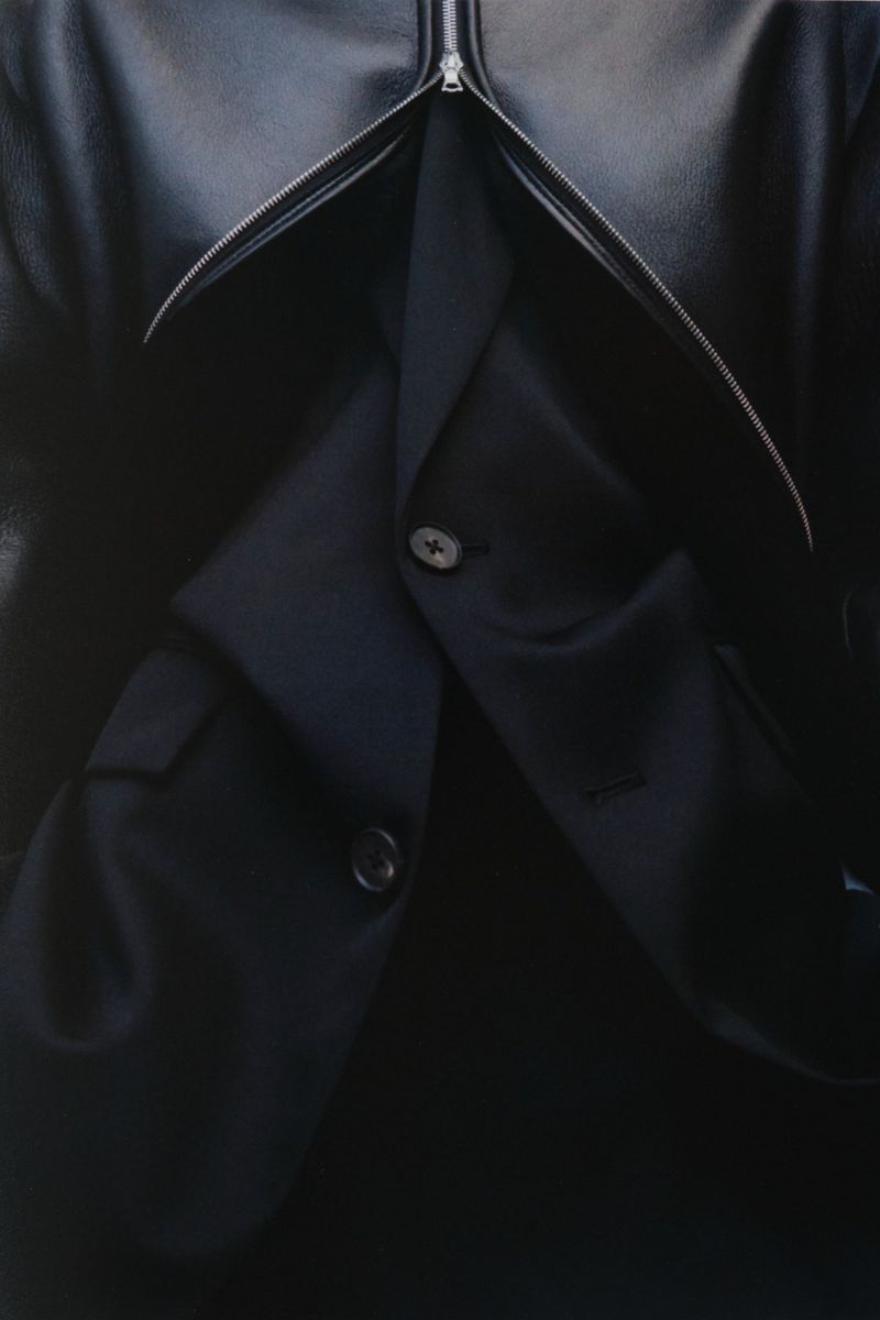 Close-up of a navy blue suit jacket under a black leather jacket with a zipper. Dark, fashionable outerwear, layered clothing.