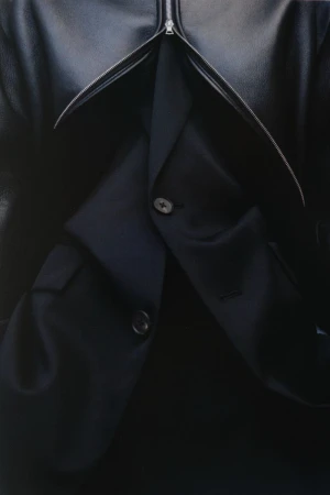 Close up of layered dark clothing featuring an unzipped black jacket over a blazer with visible buttons.