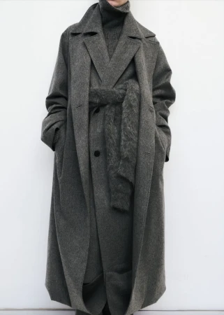 Model wearing a grey wool trench coat and matching turtleneck against a clean white seamless studio background.
