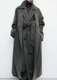 Model wearing a grey wool trench coat and matching turtleneck against a clean white seamless studio background.