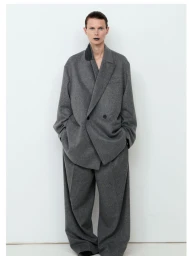Model wearing an oversized grey wool suit with dark lipstick against a plain white studio background
