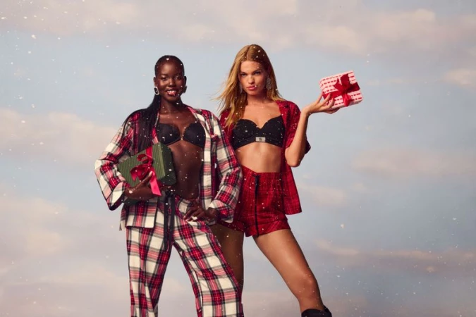 Adut Akech and Daphne Groeneveld holding wrapped holiday gifts under falling snow for Victoria's Secret Holiday campaign.