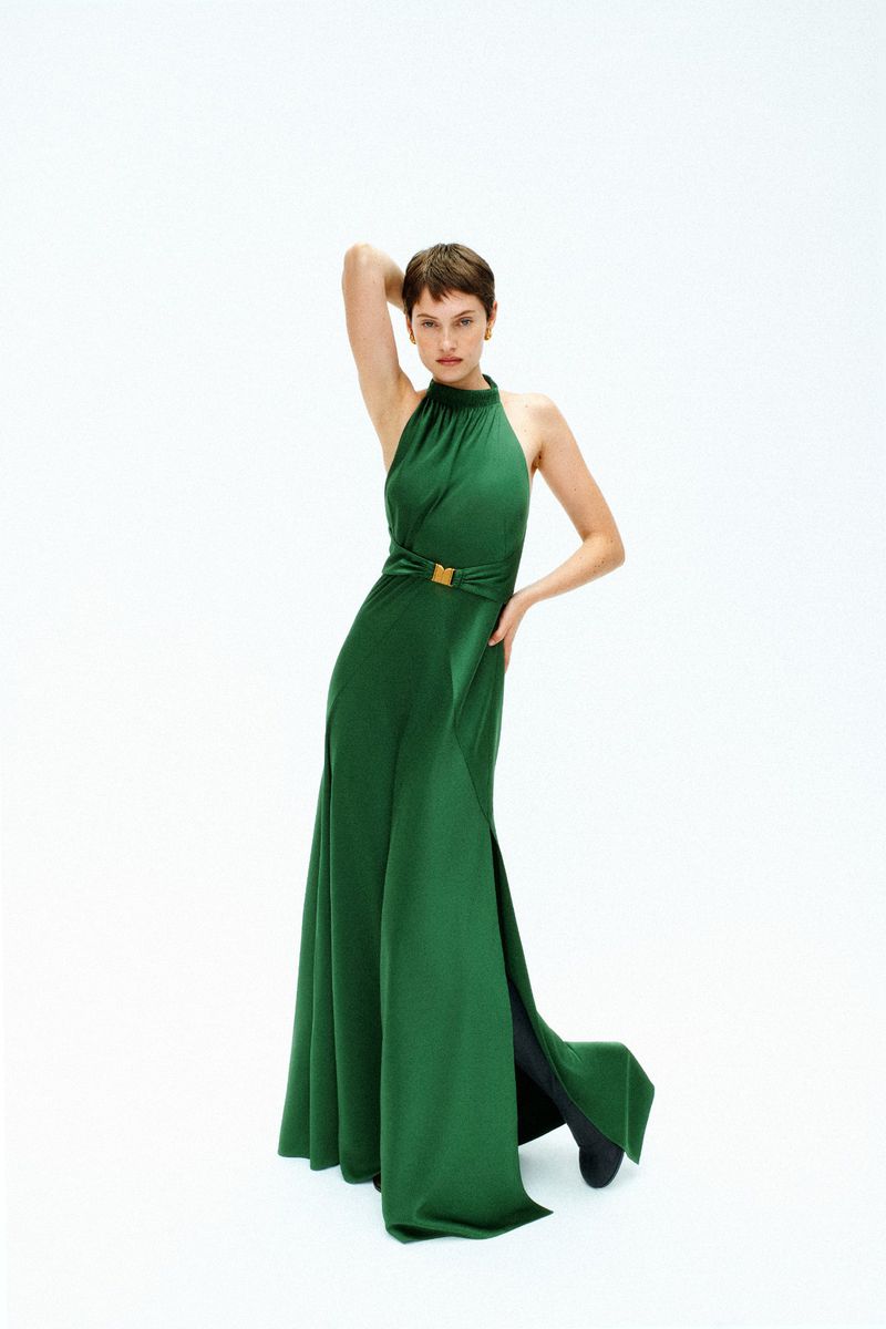 Model with short brown hair wearing a long green halter dress against a plain white background