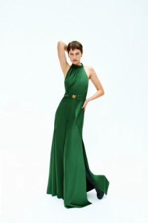 Model with short brown hair wearing a long green halter dress against a plain white background