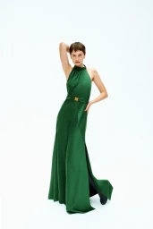 Model with short brown hair wearing a long green halter dress against a plain white background