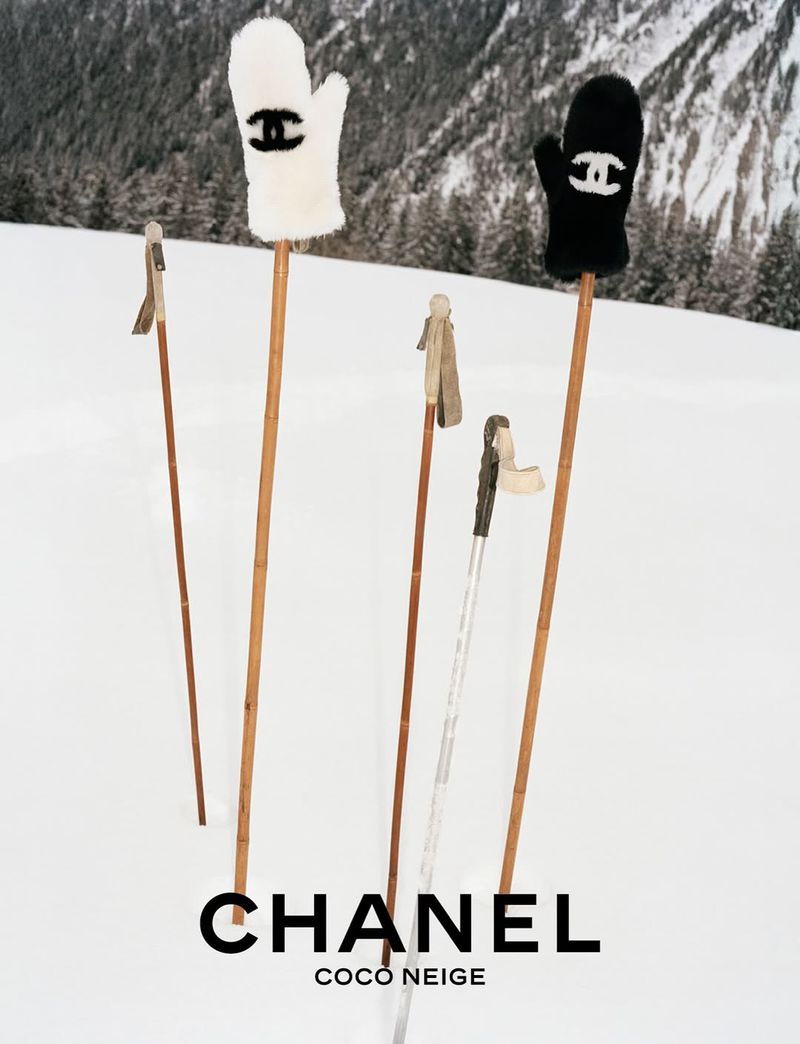 Chanel COCO NEIGE fashion ad featuring mittens on ski poles stuck in snow in a winter landscape with pine trees in the background.