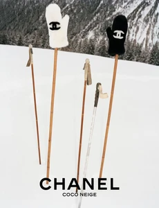White and black shearling mittens with logo perched on ski poles planted in a snowy alpine landscape