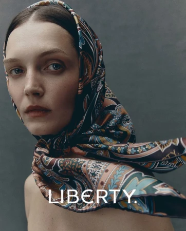 Close-up portrait of a woman wearing a patterned scarf as a head covering, shot in a studio with a grey background and natural lighting.