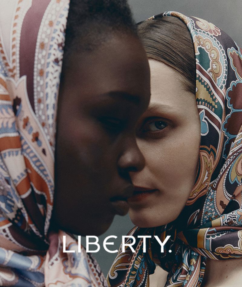 Close-up of two women with paisley headscarves. One woman has dark skin, and the other has fair skin, both with neutral expressions.