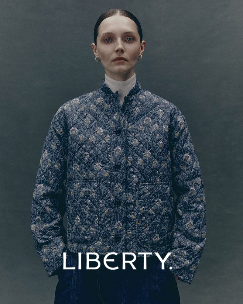 Woman in a Liberty-print quilted jacket stands in a studio with medium lighting. Fashion portrait showcasing textile detail.