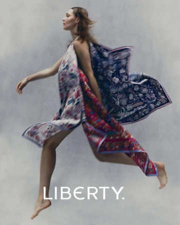 Model leaping in motion wearing a patterned floral dress against a textured grey studio background