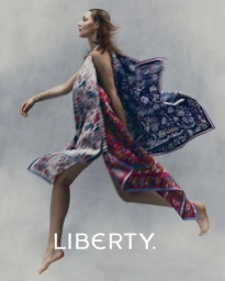 Model leaping in motion wearing a patterned floral dress against a textured grey studio background