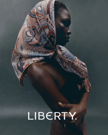 Black woman wearing a patterned pink and blue silk headscarf in profile against a dark grey background for Liberty FW25