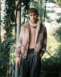 Model wearing a striped knitted cardigan and scarf outdoors against a natural forest background