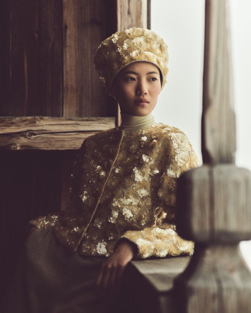 Asian woman poses in embroidered hat and matching jacket in a soft window light. Fashion editorial photography, natural and elegant.