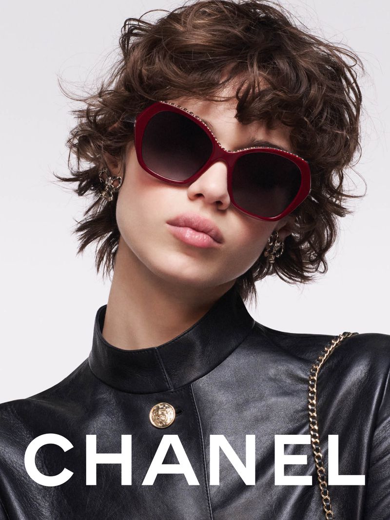 Model wearing dark red sunglasses and a black leather jacket against a white background for Chanel Eyewear.