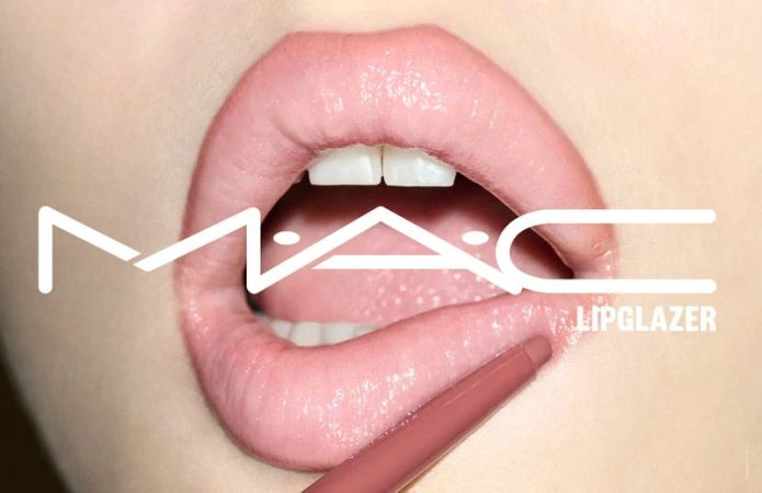 Macro shot of glossy lips being lined with a nude lip pencil, showcasing a close-up of teeth and a MAC Lipglazer logo.