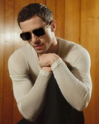 Man wearing designer sunglasses and white ribbed sweater against wooden wall panels for Versace eyewear campaign