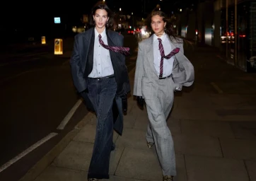 Two models in tailored suits and ties walking down a city street at night for the H and M autumn winter 2025 campaign.